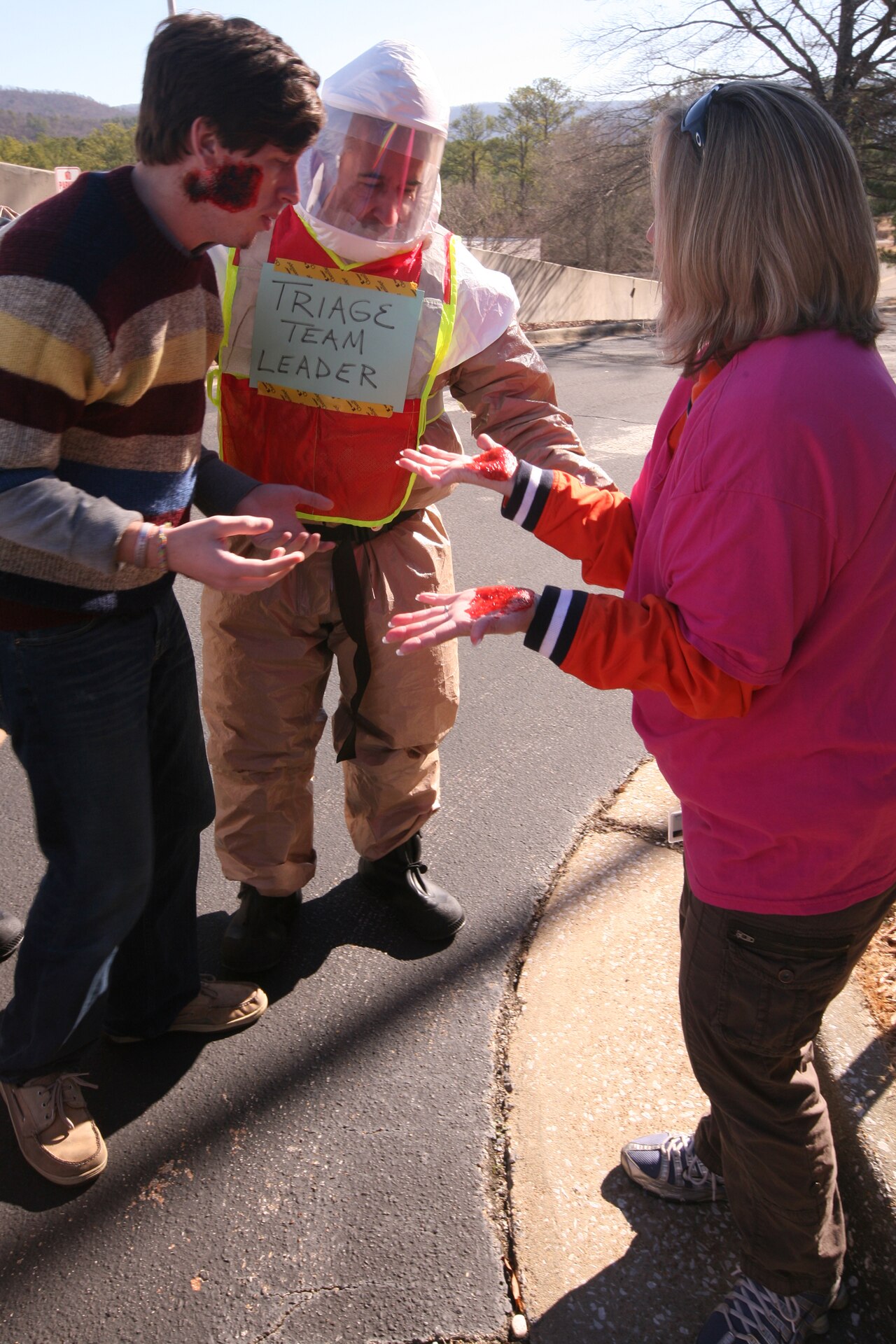 Triage team leader in protective gear assessing volunteers with simulated wounds during an exercise