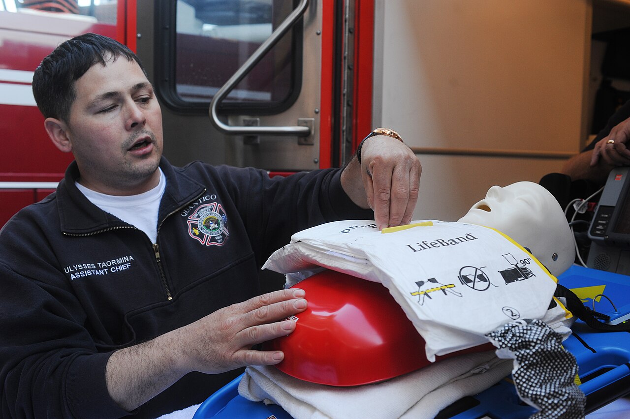 Folded LifeBand band-type chest device on a training manikin, with a fire department officer explaining it
