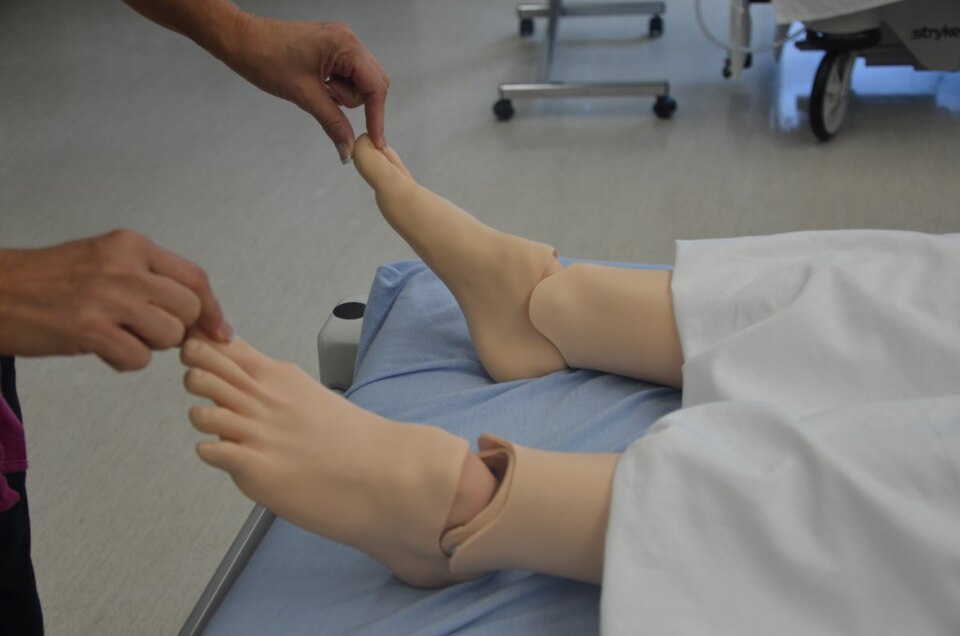 Clinician pressing the toe of a training manikin to test capillary refill