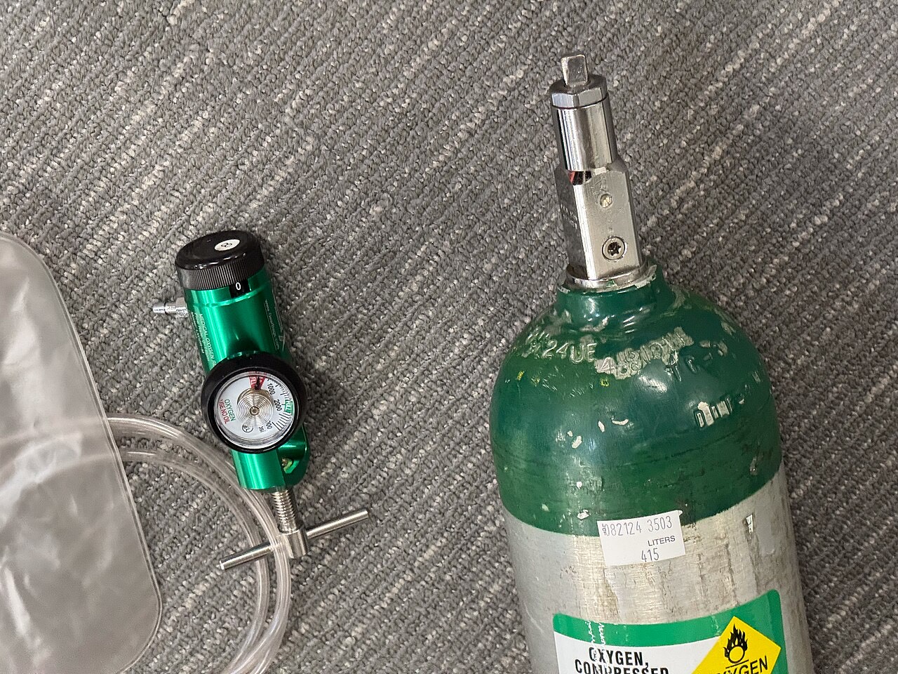 Green oxygen cylinder labeled 415 liters beside a post-valve regulator with pressure gauge and flow dial